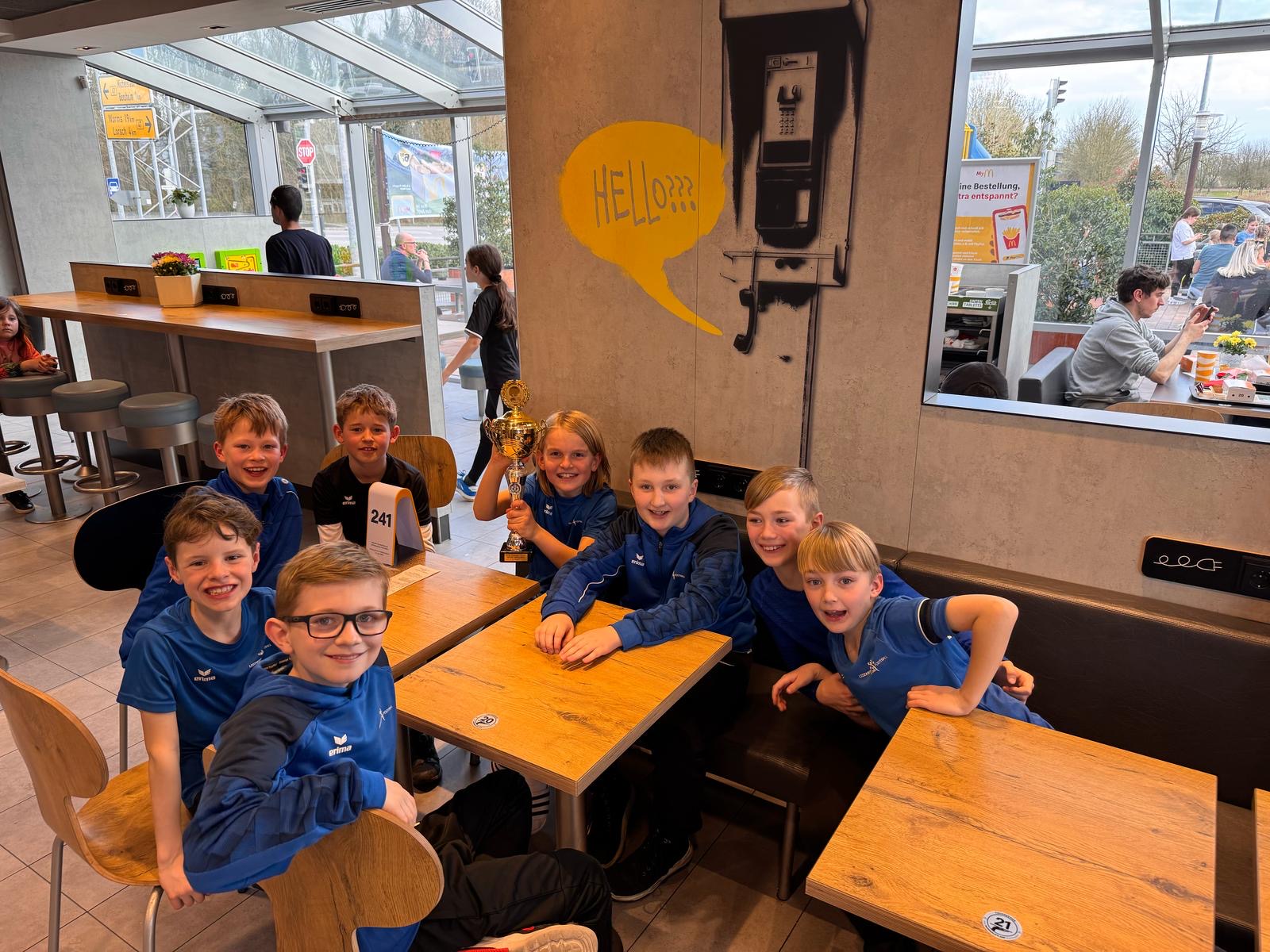 Spieler mit strahlendem Lächeln, die nach dem Spiel den Pokal in den Händen halten, während sie in einem Restaurant auf ihr Essen warten.