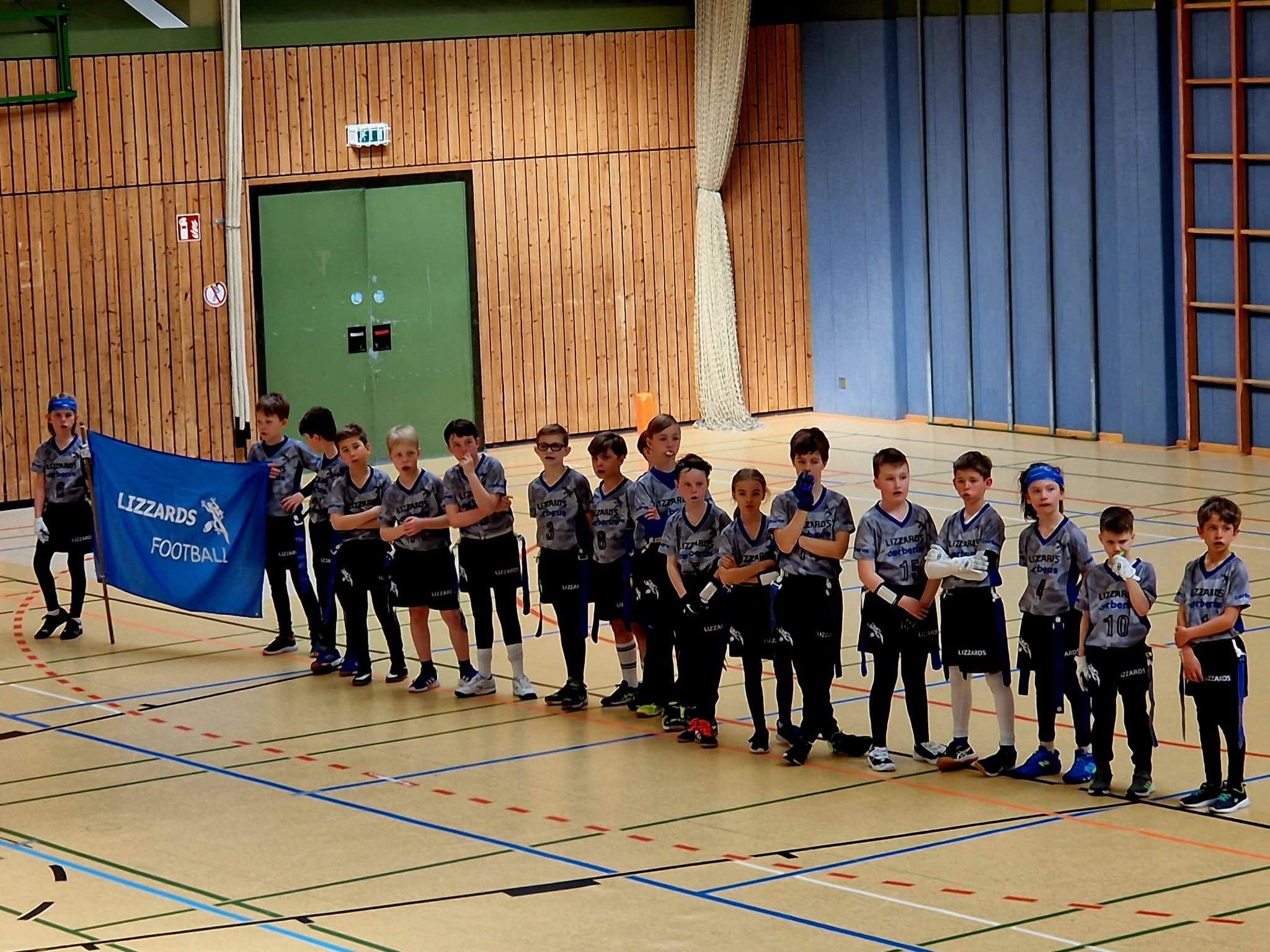 Juniors U10 players standing in a que with two boys holding a blue banner saying 'Lizzards Football' on the extreme left of the photo.